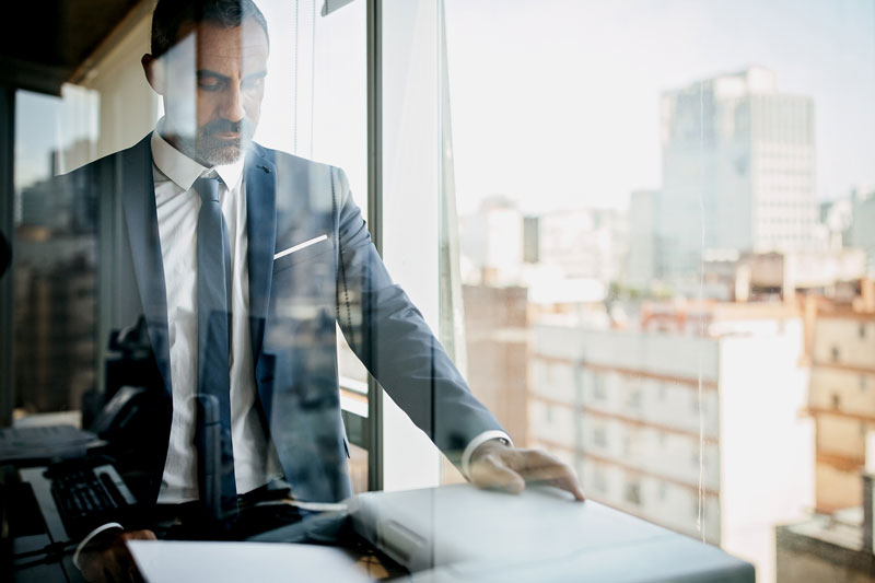 man in suit stands over printer with a city view background